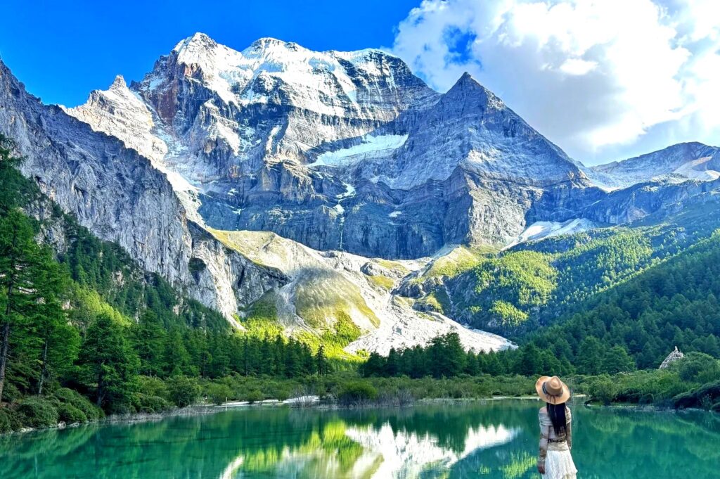 云南四川12日深度游封面，稻城亚丁仙乃日雪峰倒映翠绿高山湖，旅人伫立眺望神山圣域