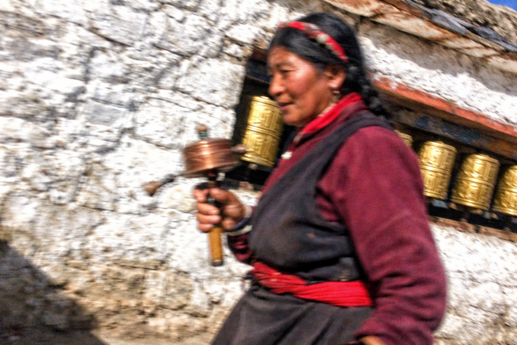 扎什伦布寺转经道,藏族妇女手持转经筒绕寺而行,白墙与金色经筒在午后阳光下交错,日喀则格鲁派寺院日常朝圣景象。