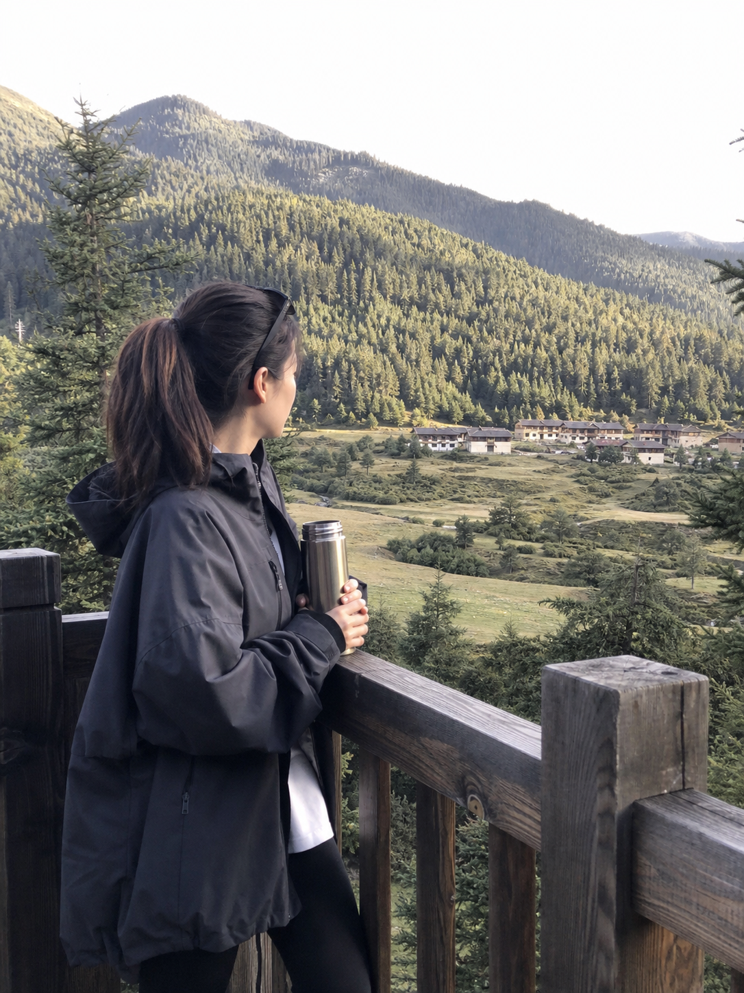 鲁朗林海观景台上旅人拿著保温杯眺望森林、草甸与藏式村落,林芝鲁朗一日游景点